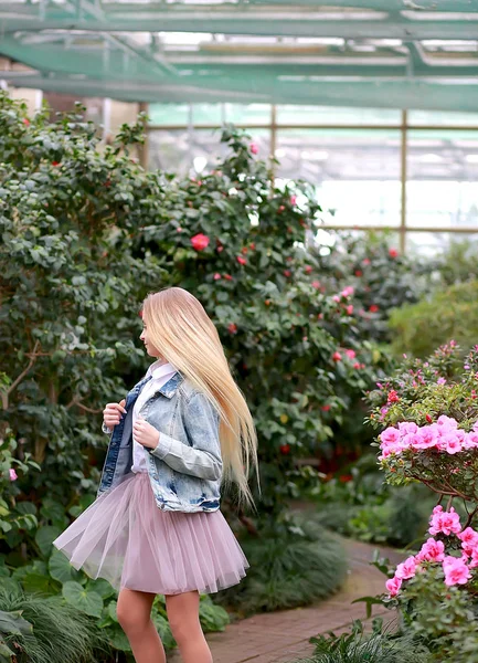 デニムジャケットを着た長い白い髪の少女が花の中を歩く — ストック写真