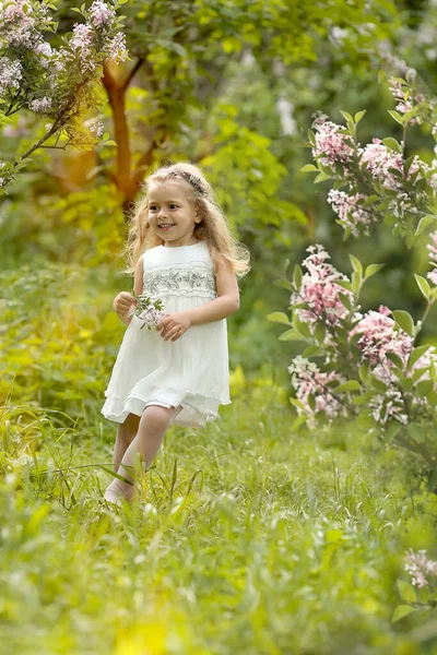 Klein meisje in een witte jurk wandelingen in de lente botanische tuin — Stockfoto