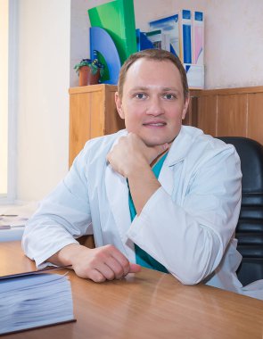 Doktor bey işyerindeki masada oturuyor ve gülümsüyor. 