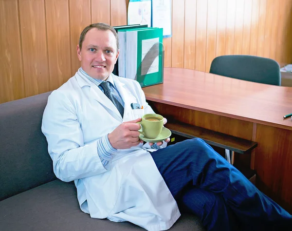 Молодой привлекательный врач в белом халате держит чашку кофе — стоковое фото