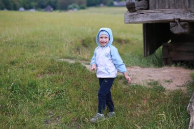 Çocuk mavi şapkalı ve rüzgarlık giymiş bir şekilde doğada ailesiyle yürüyor.