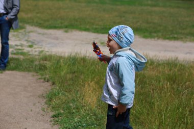 Çocuk mavi şapkalı ve rüzgarlık giymiş bir şekilde doğada ailesiyle yürüyor.
