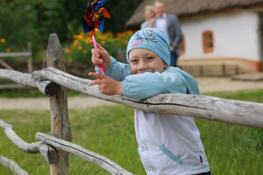 Çocuk mavi şapkalı ve rüzgarlık giymiş bir şekilde doğada ailesiyle yürüyor.