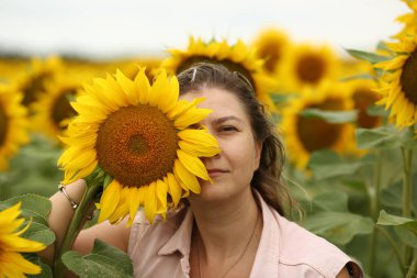 Sarı ayçiçeklerinin açtığı tarlada hasır şapkalı genç bir kadın. Tarım konsepti. Ayçiçeği yağı üretimi.