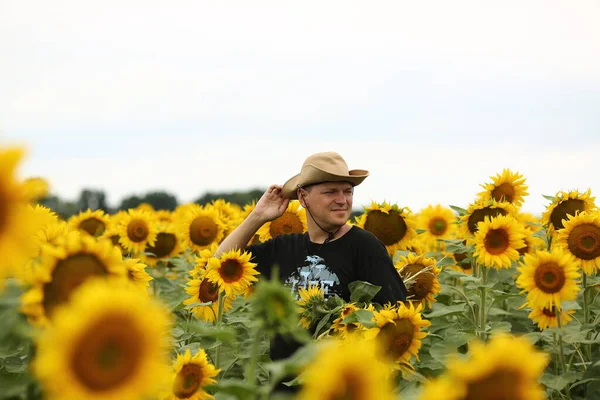 Young male farmer in a hat in a field where yellow sunflowers are blooming. Agriculture concept. Sunflower oil production.