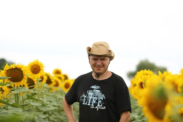 Young male farmer in a hat in a field where yellow sunflowers are blooming. Agriculture concept. Sunflower oil production.