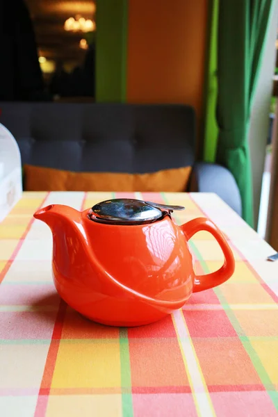 Bright red modern ceramic teapot isolated on a colored checkered tablecloth. The restaurant is cozy. Tea ceremony. Healthy eating concept. Design and interiors.