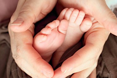 Yeni doğmuş bir bebeğin bebek bacakları annelerin ellerinde, makro çekim. Annesi ve bebeği. Doğumhane. Mutlu aile kavramı. Anneliğin güzel kavramsal görüntüsü. Anneler Günü.
