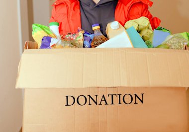 Volunteer young Caucasian guy in a protective medical mask and gloves with a donation box with food. Close-up. Home insulation. Coronavirus 2019-nkov. Donation. Delivery. Food. Volunteer clipart