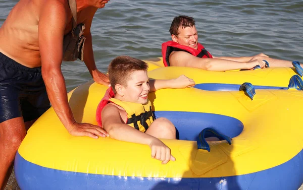 Kırmızı can yelekli baba ve oğlu şişirilebilir sarı bir tüple denizde birlikte seyahat ediyorlar. Ekstrem Spor. Adrenalin. Yaz eğlencesi ve etkileyici hız pateni. Aktif yaşam tarzı. Mutlu aile kavramı