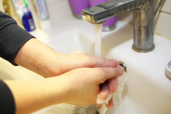 Wash hands with soap under a tap with water close-up. Hygiene concept. To prevent the coronavirus pandemic. A young boy washes his hands with soap in the bathroom at home