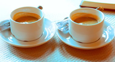 Bir kafede, bir fincan çay tabağının üzerinde iki fincan beyaz kahve, şeker, bir defterin yanında. İki kişilik kahvaltı. - Günaydın. Sevgi. Alışkanlıklar. İş adamları. Gurme. Kahve severler. Kahveci. Yakın plan.