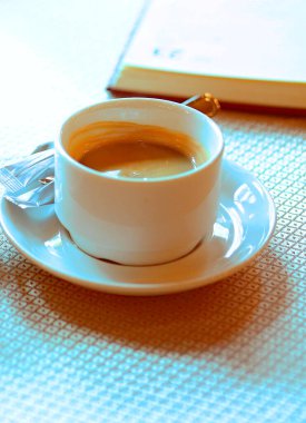 Bir fincan fincan fincan tabağında bir fincan beyaz kahve bir kafede masanın üzerinde duruyor, iki poşet şeker, bir defterin yanında. Kahvaltıda. - Günaydın. İş adamları. Gurme. Kahve severler. Kahveci. Kafeler ve restoranlar.