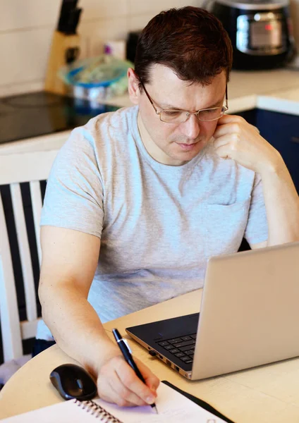 Work at home online during a pandemic 2019-ncov. Focused and serious young man in glasses takes some notes while sitting at his workplace. Online Job Concept. Self-isolation