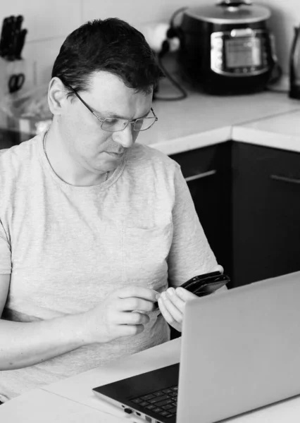 Work at home online during a pandemic 2019-ncov. Serious young man in glasses calls on a mobile phone at work sitting at his workplace. Close-up. Online Job Concept. Self-isolation