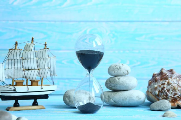 Banner with beach accessories on a blue board aquamarine color background - hourglass, boat, sea stones. Summer. Concept of summer holidays. Vacation and Travel Time Concept.