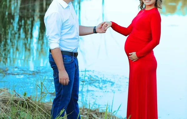 Married couple. Pregnant woman in a red dress and man in a white shirt and jeans on the lake. Love, family, pregnancy. The concept of a happy marriage and family. Copy space on the left
