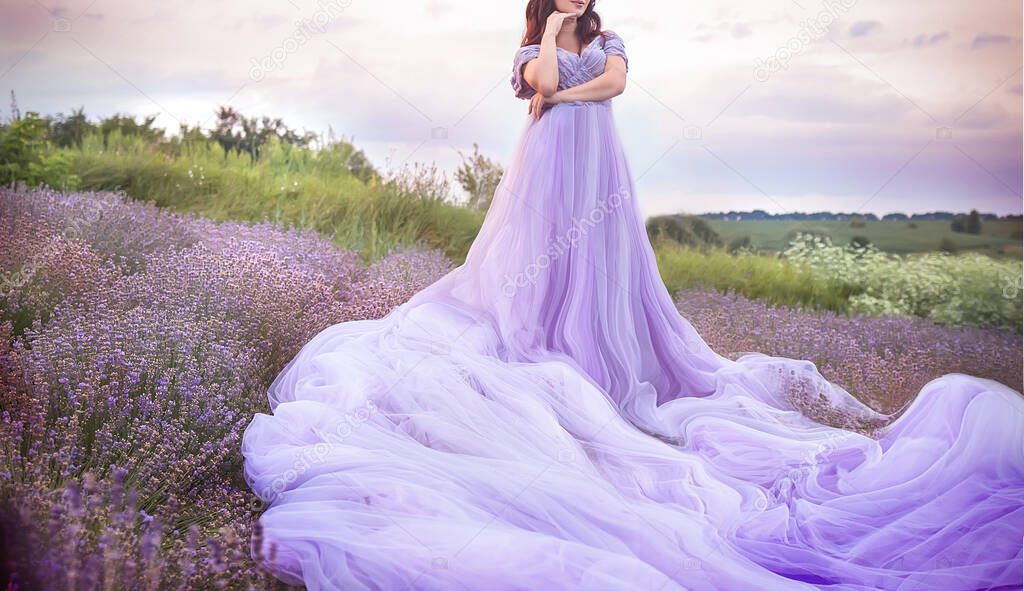 A gorgeous young girl in a fashionable lilac dress of tulle in a lavender field walks at sunset. Provence, Lavender, France. Beautiful summer concept.