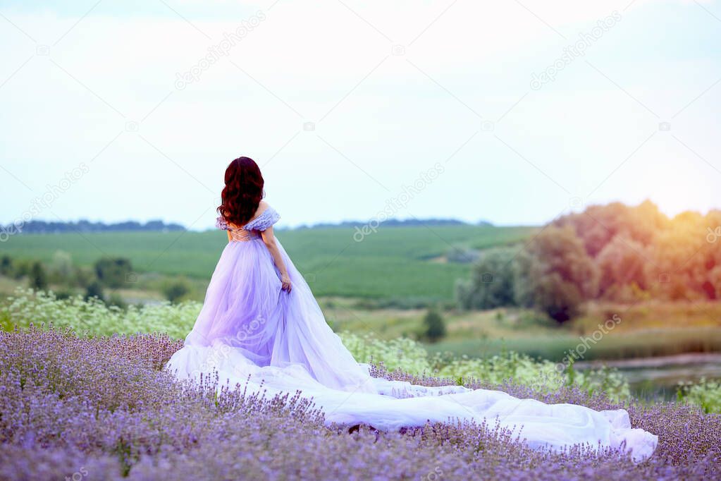 A gorgeous young girl in a fashionable lilac dress of tulle in a lavender field walks at sunset. Provence, Lavender, France. Beautiful summer concept.