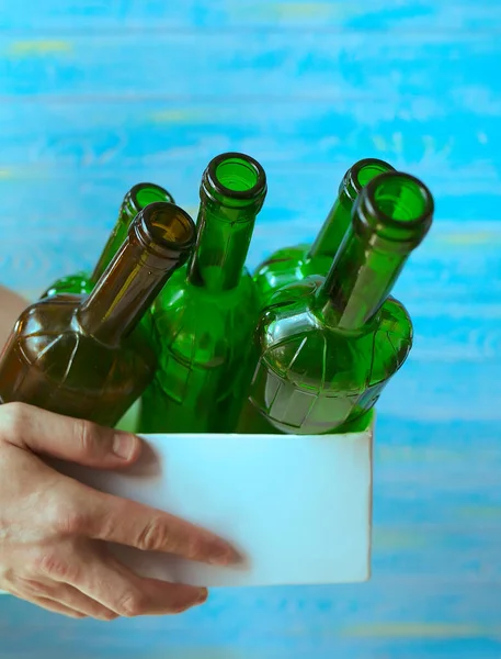 Sorting garbage and waste. A man holds a box with glass bottles for recycling on a blue background. Stop plastic. Ecology. Recycling concept. Zero waste. Close-up