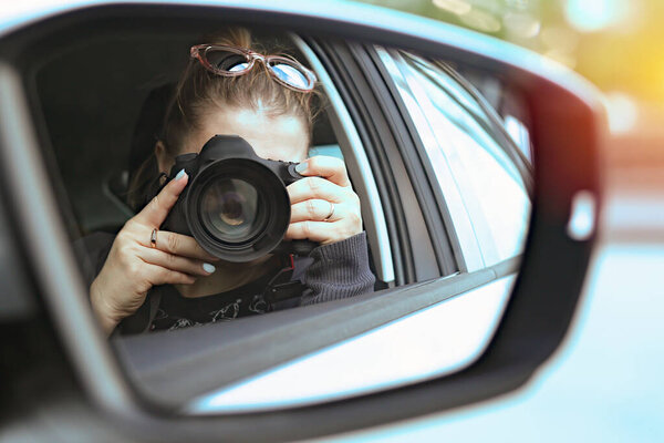 Portrait of a photographer covered her face with a camera while sitting in a car from a window photographing people on the street. At work. Lens close-up. Photo in the mirror of a car. Report Concep