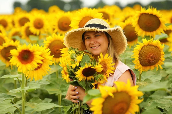 woman in a field with a bouquet of sunflowers and a straw hat, portrait, close-up. Summer concept
