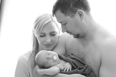 Kadın ve erkek yeni doğmuş bir bebeği tutuyor. Anne, baba ve bebek. Kollarında yeni doğmuş bir bebekle gülümseyen bir ailenin portresi. Mutlu aile kavramı.. 