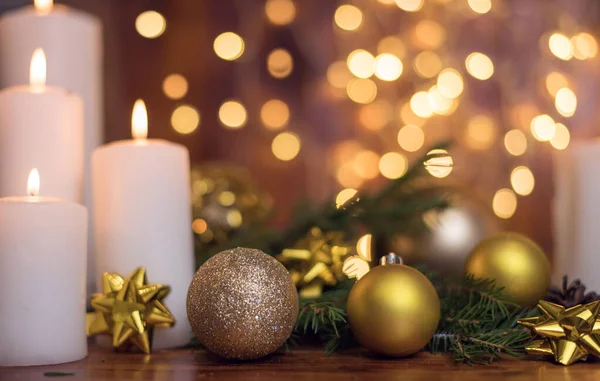 Golden Christmas ball on a tree branch, white candle flame with stars bokeh lights on a brown background Stock Photo