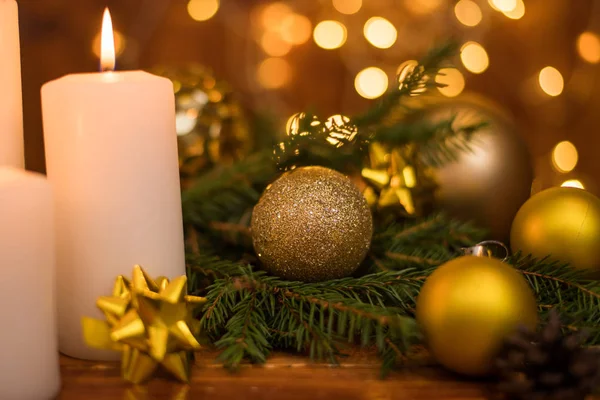 Bola de Natal dourada em um galho de árvore, chama de vela branca com luzes bokeh estrelas em um fundo marrom — Fotografia de Stock