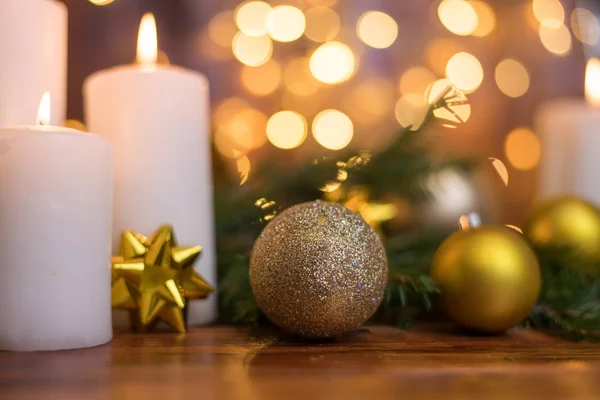 Bola de Natal dourada em um galho de árvore, chama de vela branca com luzes bokeh estrelas em um fundo marrom — Fotografia de Stock