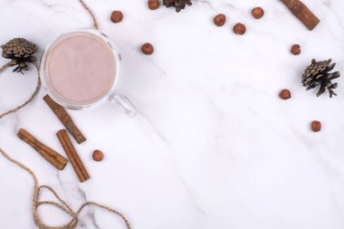 Kışlık şeylerle çevrili cam bir bardakta kakao içmek beyaz bir masada tarçın yemek. Sıcak tatil kavramı.