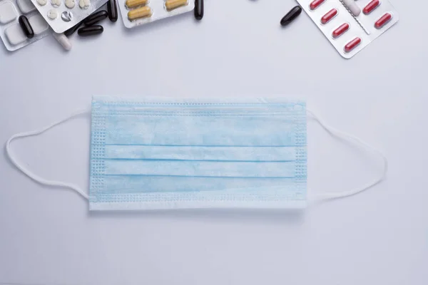 Máscara azul médica descartável, equipamento de proteção individual em backgraund branco com pílulas — Fotografia de Stock