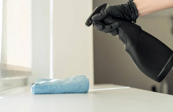 En kvinna hand i svarta handskar håller en blå mikrofiber rengöringsduk och en spray med en sterilisering gör desinfektion för god hygien — Stockfoto