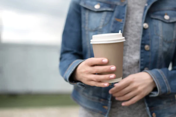 Women\'s hands in a denim jacket hold a Cup of coffee.