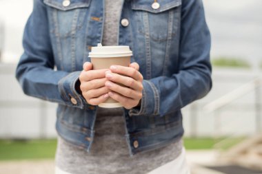 Kot ceketli kadın elleri bir fincan kahve tutuyor..