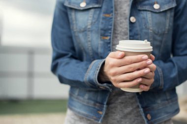 Kot ceketli kadın elleri bir fincan kahve tutuyor..