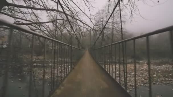 在落基河上的旧金属丝缆索桥上的飞奔在冬季雾雾天电影中的广角风景 — 图库视频影像