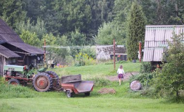 Little girl run on backyard of the rural house with old buildings and tractor in summer day