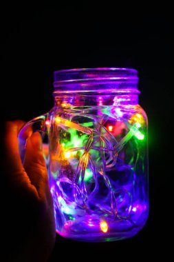 Gece karanlığında cam kavanozda parlak renkli çelenk ışıkları olan bir kart..