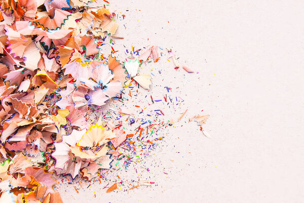 Wooden pencil shavings and colorful crumbs of graphite from sharpener on soft pink paper background. Top view. Design elements for poster, banner, cards.