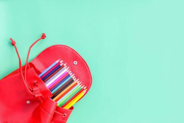 Mavi arka planda okul ekipmanları için kırmızı çanta. İçinde renkli kalemler olan okul çantası..