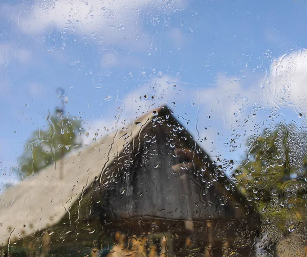 Country yard with old cowshed building behind the wet glass with autumn rain drops.