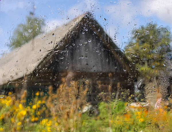 Country yard with old cowshed building behind the wet glass with autumn rain drops.