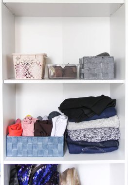 Gardıropta üzerinde kağıt notlar olan farklı kıyafetler. Küçük uzay organizasyonu. Dikey depolama. Kumaş kutularda katlanmış gömlekler..