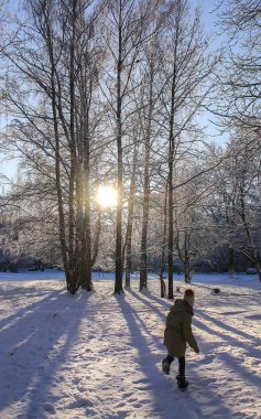 Little girl in warm coat playing in winter snow-covered park