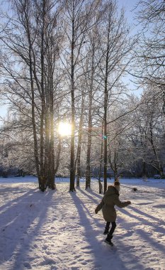 Little girl in warm coat playing in winter snow-covered park