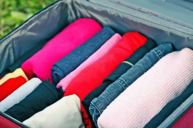 Yeşil çimlerin üzerinde farklı giysiler katlanmış bir şekilde bavulu aç. Seyahat paketinde kolay ve küçük alan tasarrufu için dikey depolama