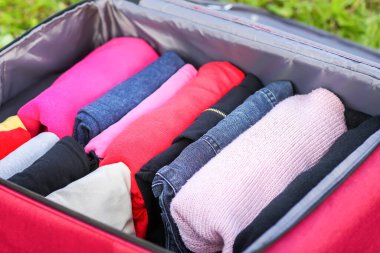 Yeşil çimlerin üzerinde farklı giysiler katlanmış bir şekilde bavulu aç. Seyahat paketinde kolay ve küçük alan tasarrufu için dikey depolama