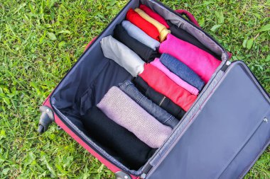Yeşil çimlerin üzerinde farklı giysiler katlanmış bir şekilde bavulu aç. Seyahat paketinde kolay ve küçük alan tasarrufu için dikey depolama