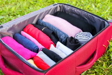 Yeşil çimlerin üzerinde farklı giysiler katlanmış bir şekilde bavulu aç. Seyahat paketinde kolay ve küçük alan tasarrufu için dikey depolama